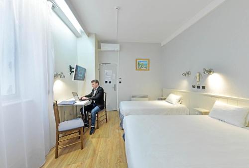 a woman sitting at a desk in a room with two beds at Hôtel Saint André Gare SNCF in Clermont-Ferrand