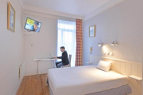 a man sitting at a desk in a hotel room at Hôtel Saint André Gare SNCF in Clermont-Ferrand