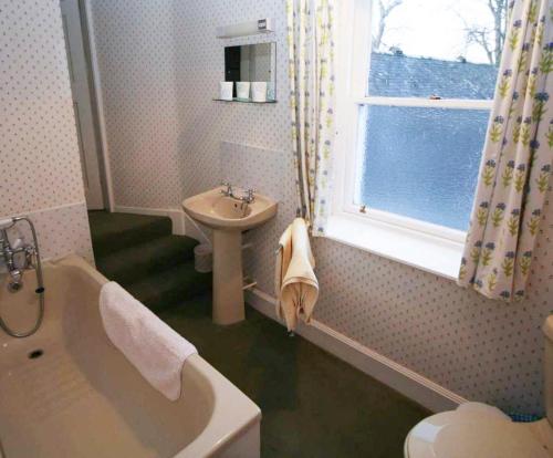 ein Bad mit einer Badewanne, einem Waschbecken und einem Fenster in der Unterkunft Georgian Farmhouse in Castle Douglas