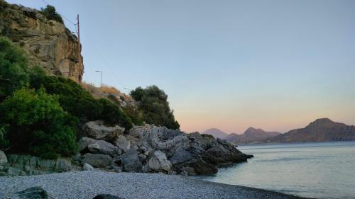 a rocky beach with the ocean and mountains in the background at Eolia beachfront studios in Plakias