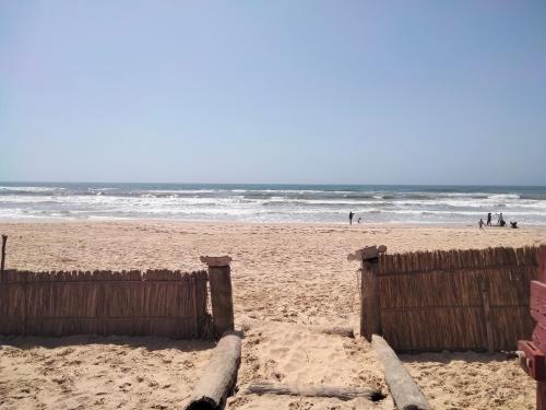 a wooden fence on a beach with people in the ocean at Gaal-Gui, chez Guillaume in Mboro