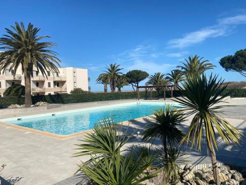 une piscine avec des palmiers et un bâtiment dans l'établissement Résidence Les Capitelles - Studio vue sur Mer, à Saint-Cyprien