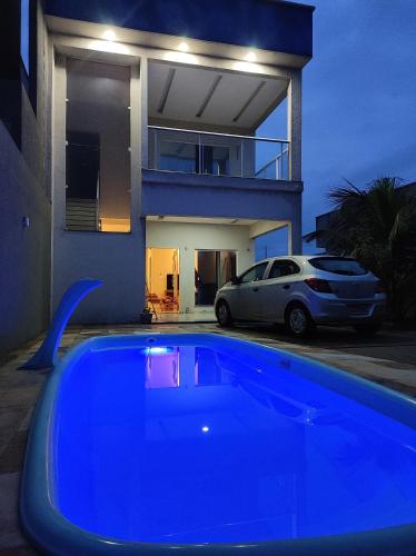 a blue pool in front of a house with a car at Casa de temporada Camocim in Camocim
