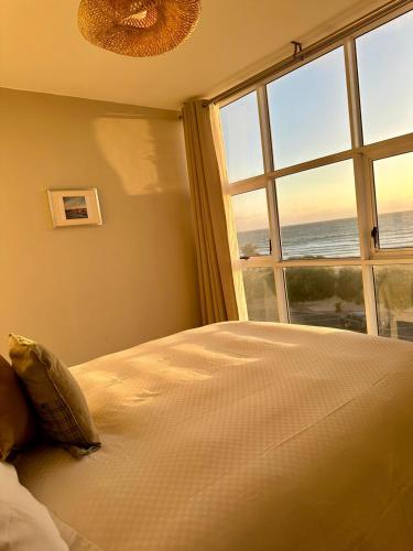 a bedroom with a large bed and a large window at Charming beachfront Strand apartment in Cape Town
