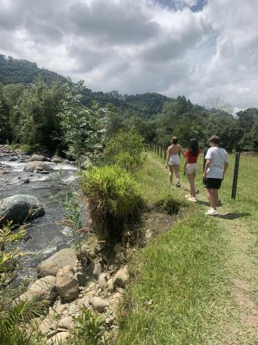 three people walking down a path next to a river at chez Yannick Hospedaje Los Amigos in Salento