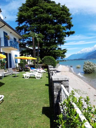 una spiaggia con tavoli e sedie, un albero e acqua di Residence Leggeri Apartments a Domaso