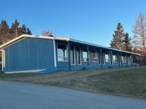 a blue building on a field next to a road at Hébergement Fort Prével in Saint-Georges-de-Malbaie
