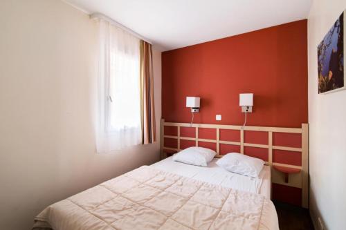 une chambre avec un lit et un mur rouge dans l'établissement Résidence le Village de Cap Esterel - maeva Home - Appartement 2 pièces 7 personnes avec coin cabine - Sélection MAE-8077, à Saint-Raphaël