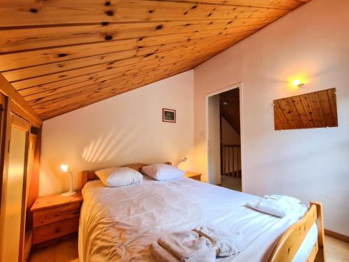 Un dormitorio con una cama con sábanas blancas y techos de madera. en Résidence Hameau - Chalets pour 8 Personnes 53, en Flaine