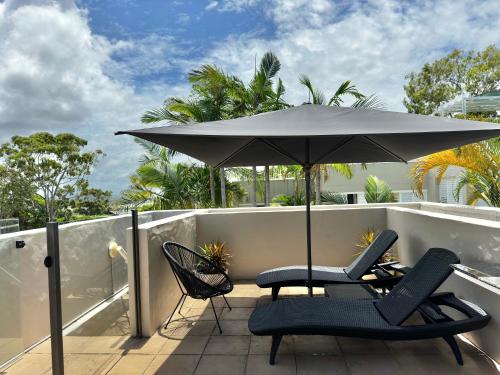 um pátio com 2 cadeiras e um guarda-sol numa varanda em Oasis Rooftop Spa Apartment em Noosa Heads