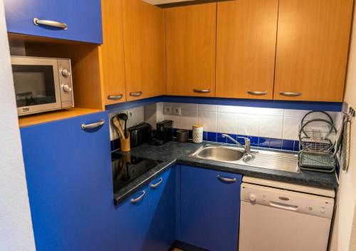 La cuisine est équipée de placards bleus, d'un évier et d'un four micro-ondes. dans l'établissement Résidence Le Parc Des Airelles - Adorable appartement avec accès direct aux pistes MAE-4221, aux Orres