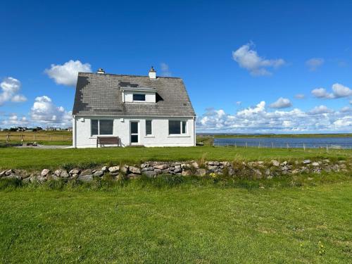 una casa bianca in un campo con un muro di pietra di Braighe Cottage a Stornoway