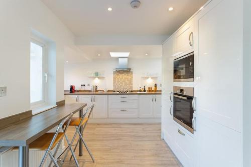 a kitchen with white cabinets and a wooden table at Modern Seaside House with Hot Tub in Earnley