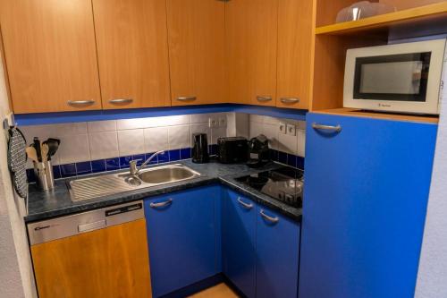 Elle comprend une petite cuisine avec des placards bleus et un four micro-ondes. dans l'établissement Résidence Le Parc Des Airelles - Magnifique T2 au pied des pistes MAE-8301, aux Orres