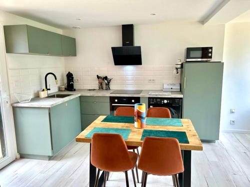 une cuisine avec une table en bois et des chaises ainsi qu'une cuisine avec des armoires vertes dans l'établissement Le Cocoon de la Héronnière, à Houlle
