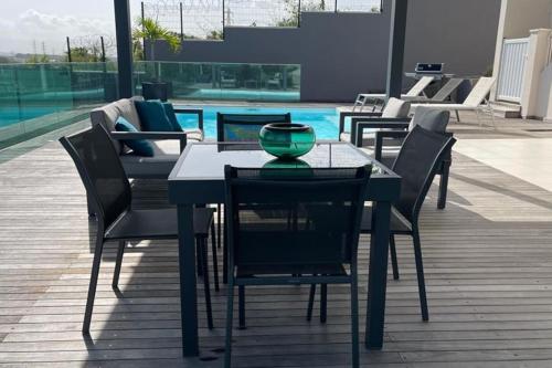 una mesa y sillas en un patio con piscina en Joli appartement cosy avec piscine, en Les Abymes