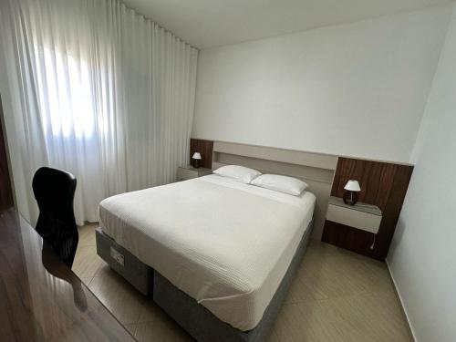 a bedroom with a white bed and a black chair at Residencial 04 Monte Carlo em São Roque in São Roque