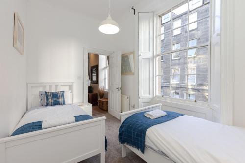 een witte slaapkamer met 2 bedden en een raam bij REFURBISHED QUIET 3 BEDROOM FLAT BY HIGH STREET, TRAMS and BUSES - 30 MINS WALK TO CENTRE in Edinburgh