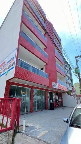 un edificio rosso e bianco con un'auto parcheggiata di fronte di Apartamento sem vista ao mar, à 15 metros da praia de Piúma a Piúma