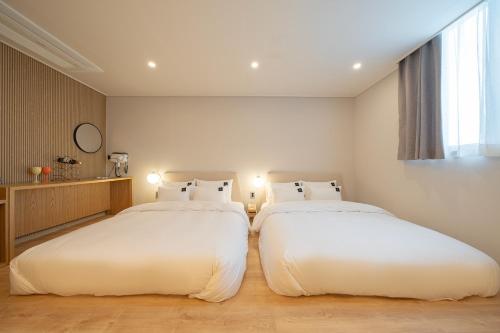 two beds in a room with white sheets at Browndot Gangneung Station in Gangneung