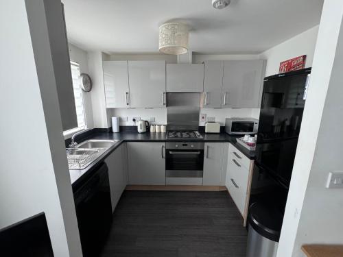una cocina con armarios blancos y electrodomésticos negros en Modern 2 bed city apartment with private parking, en Swansea