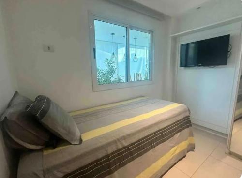 a bedroom with a bed with a window and a television at Apartamento na praia do Recreio - Posto 10 in Rio de Janeiro