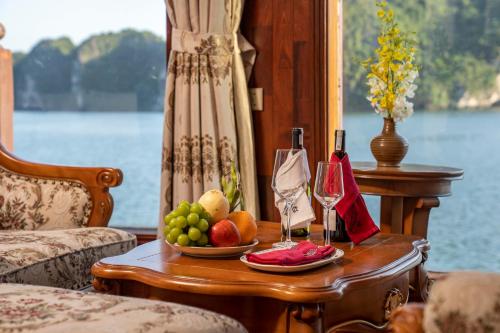 einen Tisch mit einer Schale Obst und einer Flasche Wein in der Unterkunft Emperor Cruises Legacy Ha Long in Hạ Long