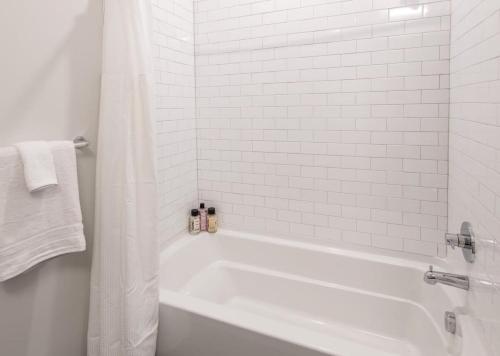 a white bathroom with a tub and a white tiled wall at Cozysuites l Modern 1BR in Downtown Cincinnati in Cincinnati