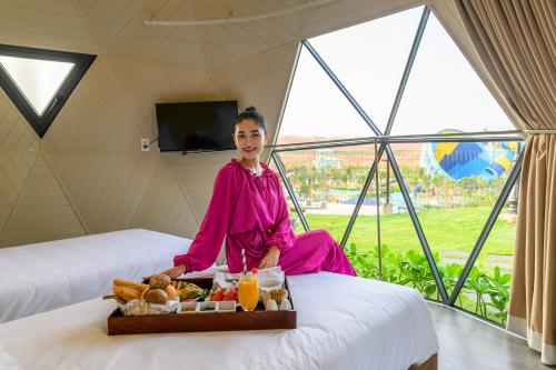 uma mulher sentada numa cama com uma bandeja de comida em Wonderland Resort Phan Thiet em Phan Thiet