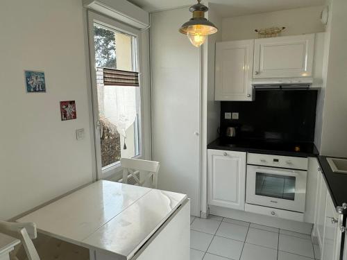 une cuisine avec des armoires blanches et un four à plaques de cuisson dans l'établissement Appartement Moderne T2, Rez-de-Jardin, Proche Plage et Centre Ville, Parking, Wifi, Animaux Acceptés - FR-1-487-362, à Cabourg