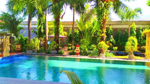 a swimming pool with palm trees and a building at Puri Saron Denpasar Hotel in Denpasar