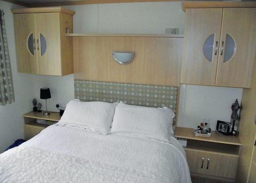 a bedroom with a white bed and wooden cabinets at Rowanbank Caravan Park in Beckfoot