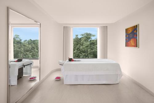 a white bedroom with a large bed and a mirror at Aurika, Mumbai International Airport - Luxury by Lemon Tree Hotels in Mumbai