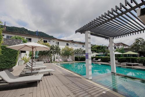 a swimming pool with chairs and an umbrella next to a building at The Melody Phuket - SHA Extra Plus in Kata Beach