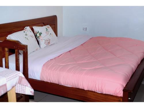 a bed with a wooden frame and pink sheets and pillows at Planete Hotel in Rubavu