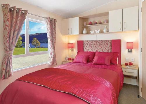 a bedroom with a large red bed with a window at Sunbeach Holiday Park in Llwyngwril