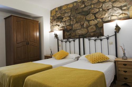 2 camas en un dormitorio con pared de piedra en Posada la Estela de Barros en Los Corrales de Buelna