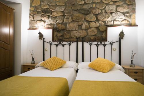 2 camas en un dormitorio con pared de piedra en Posada la Estela de Barros, en Los Corrales de Buelna