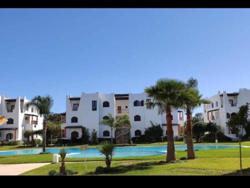 a large apartment complex with a swimming pool and palm trees at Appartement Cassia situé à Cabo Negro in Tetouan