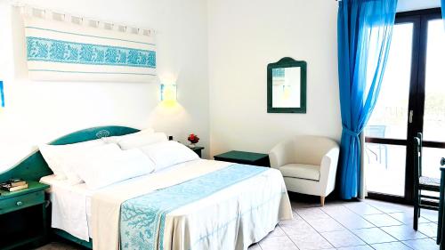 a bedroom with a bed and a chair and a window at La Perla Hotel in SantʼAnna Arresi