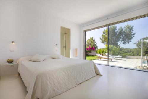 Dormitorio blanco con cama y ventana grande en Casa Flopos - Ibiza, en Nuestra Señora de Jesús