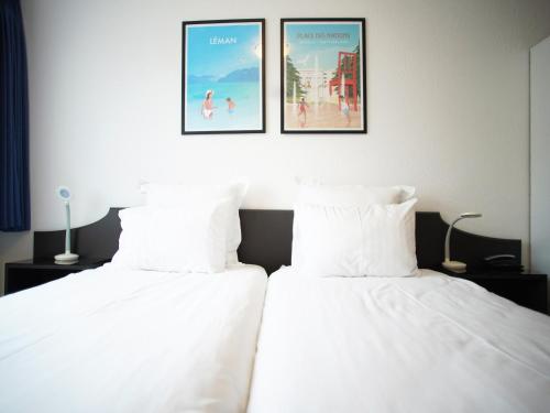 two beds with white sheets and two pictures on the wall at Primadom Aparthotel in Geneva