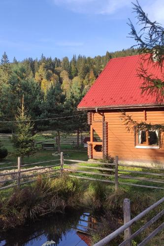 uma cabana de madeira com um telhado vermelho ao lado de um lago em Садиба Урочище Луг em Vorokhta