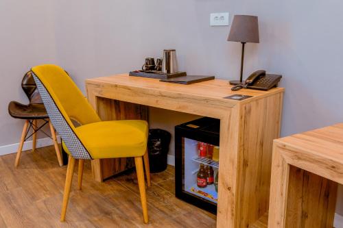 einen Holzschreibtisch mit einem gelben Stuhl neben einem Kühlschrank in der Unterkunft Nobel Gallery Hotel in Belgrad