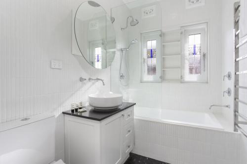 ein weißes Badezimmer mit einem Waschbecken, einer Badewanne und einem Spiegel in der Unterkunft Coastal Living Just Metres From Coogee Beach in Sydney