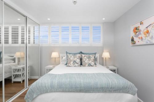 a white bedroom with a bed and two lamps at Modern Manly Apartment with Stunning Views, Pool in Sydney