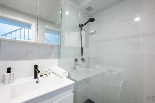 a white bathroom with a shower and a sink at Sublime Locale with Skyline Views from Courtyard in Sydney