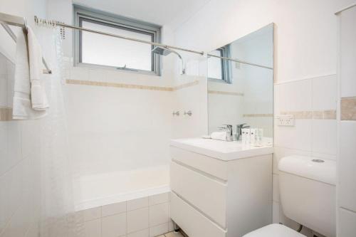 a white bathroom with a sink and a toilet at Chic Beachside Apartment Freshwater in Freshwater