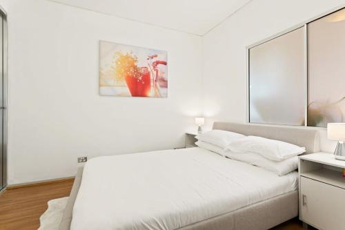 a white bedroom with a bed and a painting on the wall at Modern 1-Bed in CBD with Views near Chinatown in Sydney