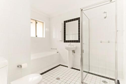 uma casa de banho branca com um chuveiro e um lavatório. em Pristine 2-Bed Near Marrickville Village em Sydney